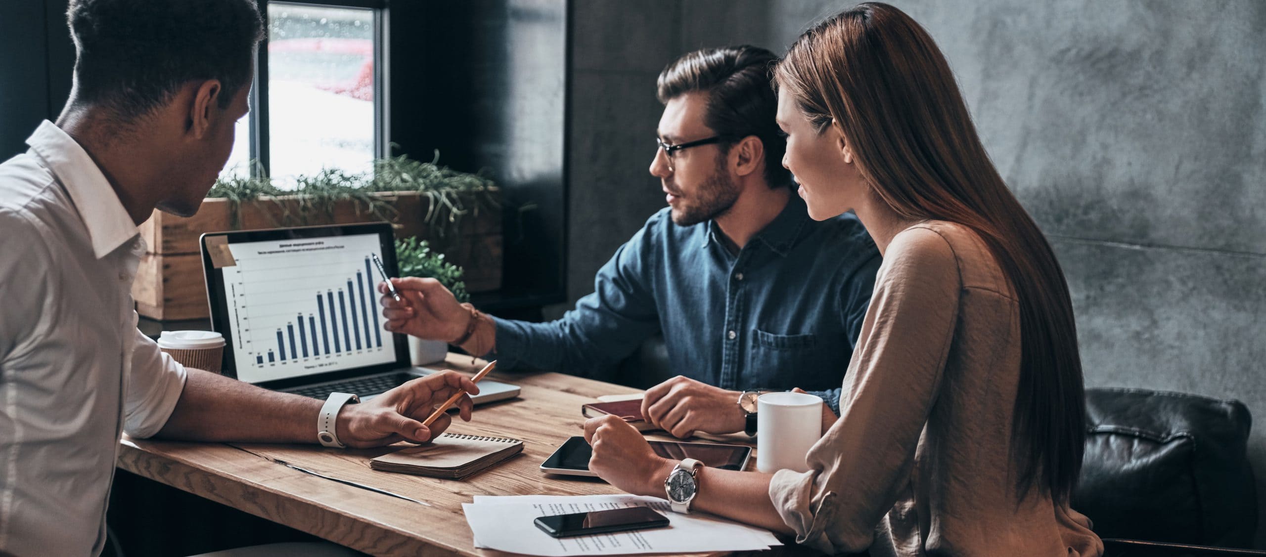 Three businesspeople gather around a desk and look at a computer monitor.