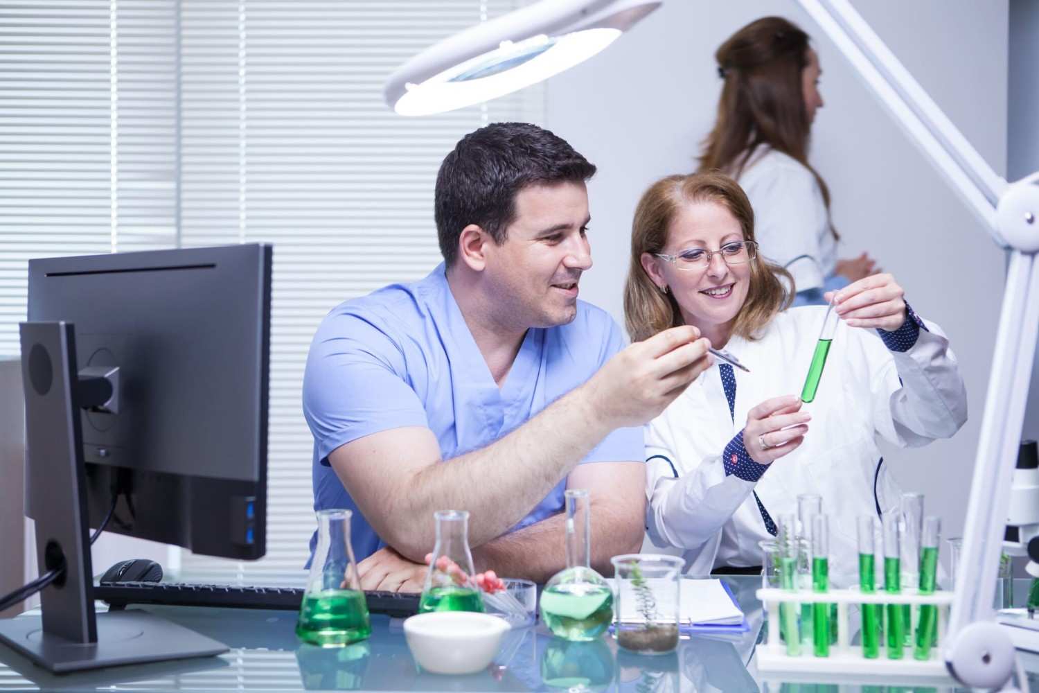 Two scientists sit at a desk and observe a test tube.