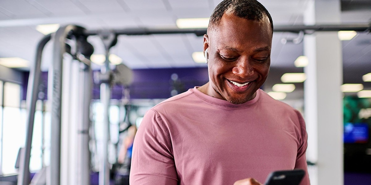 A man at the gym smiles while looking at his phone.