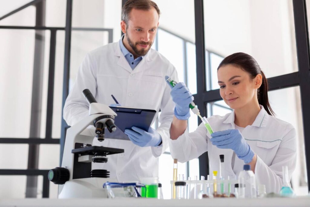 Two scientists in lab coats fill test tubes.