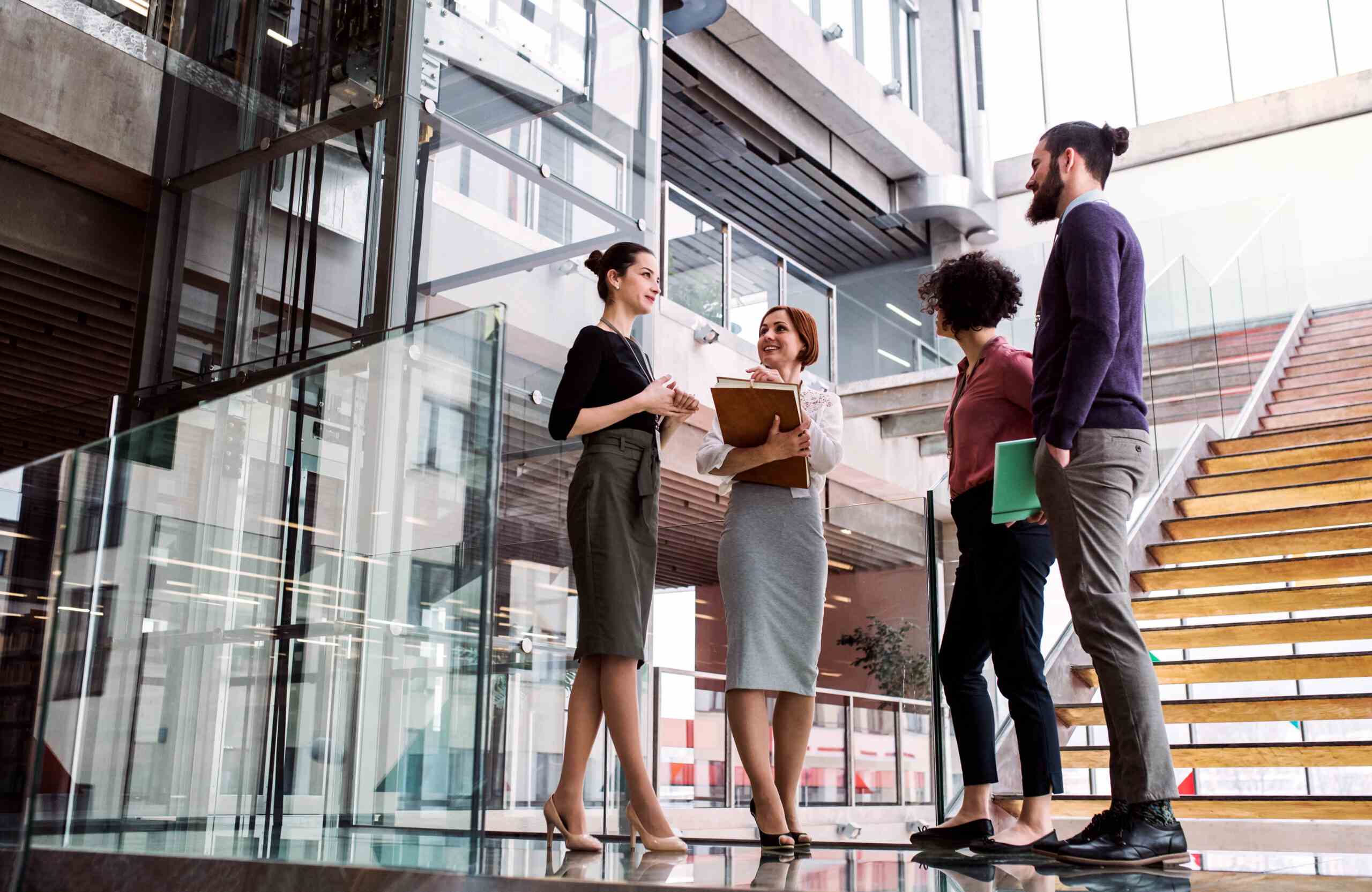 A group of people in business attire stand in a circle at the bottom of a set of stairs.