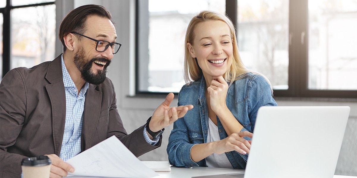 A man and a woman in business attire smile while on a video call.