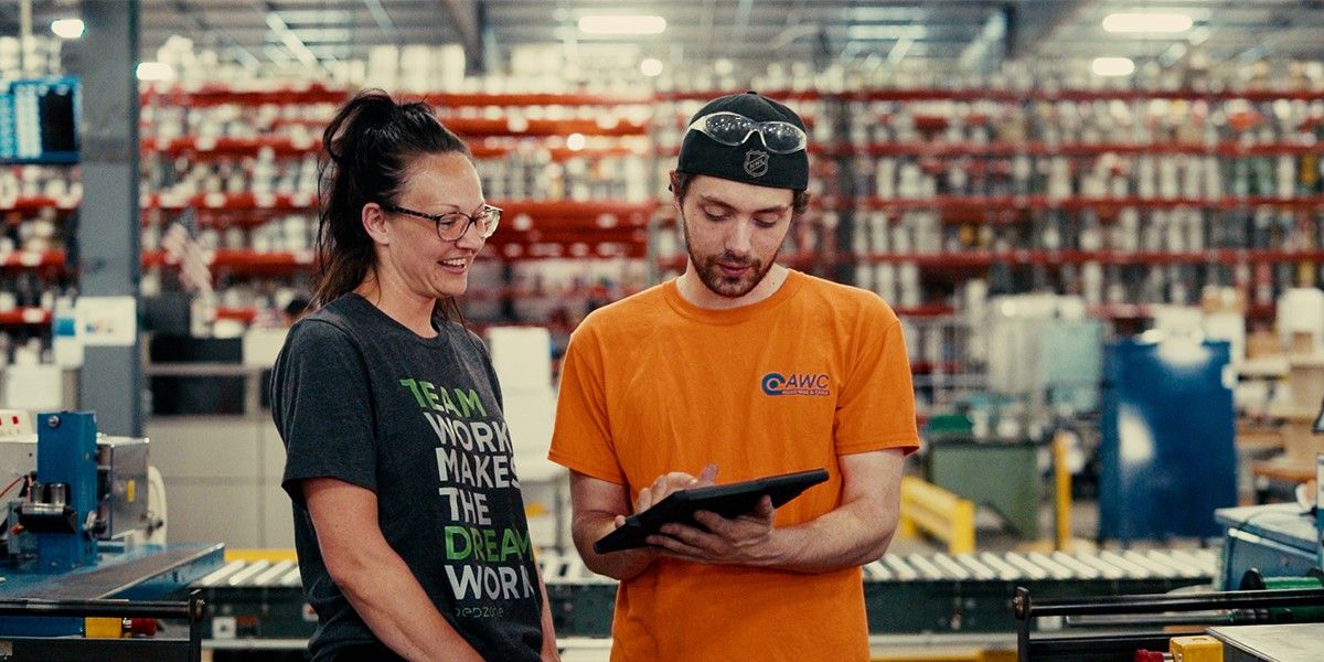 Two technicians at an assembly line take notes on a clipboard.