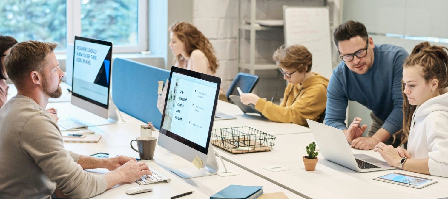 A group of tutors sit with children at a long desk.