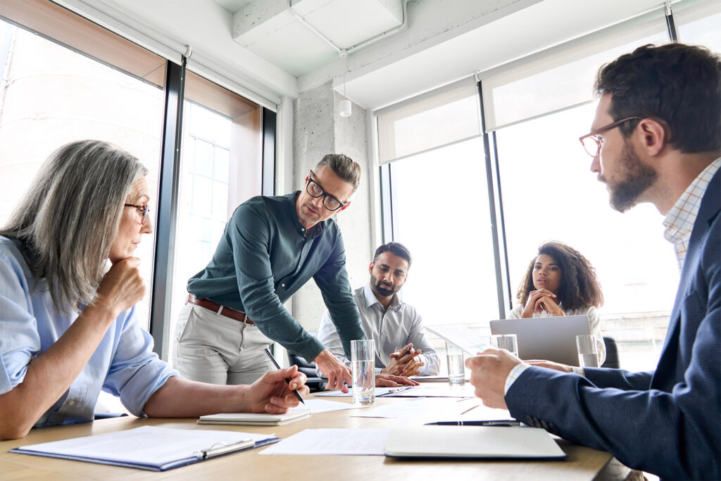 Five businesspeople discuss ideas around a meeting table.