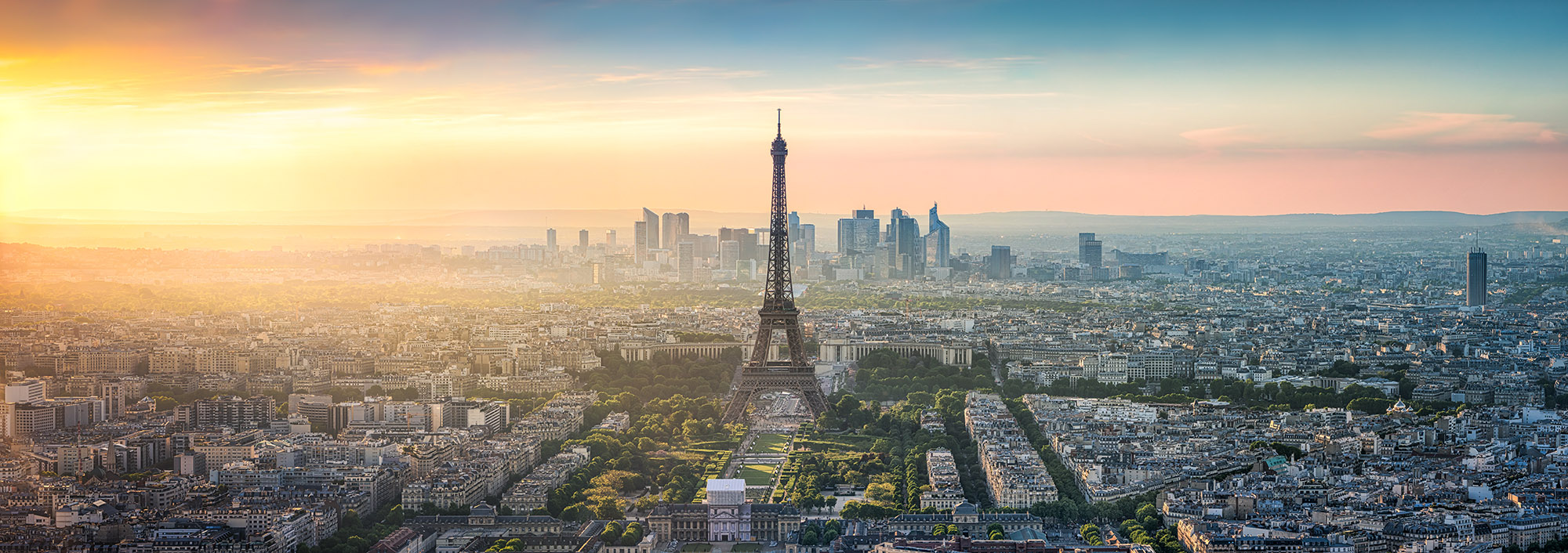 An aerial view of the Paris skyline at dusk, with the Eiffel Tower prominently centered.