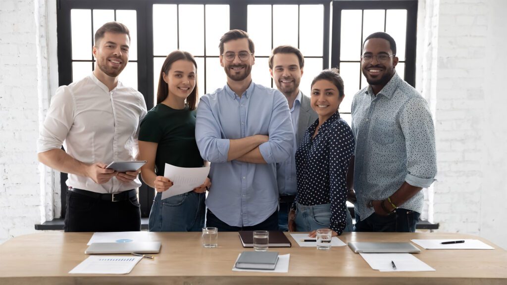 A diverse group of businesspeople pose behind a desk for a photo.