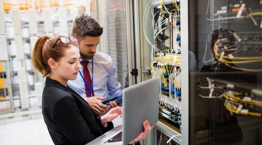 Technicians using laptop while analyzing server in server room