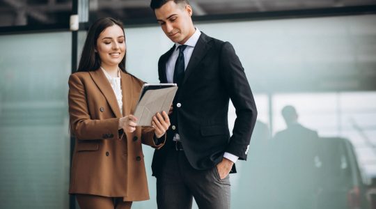 A man and woman in business attire go over notes in a notebook.