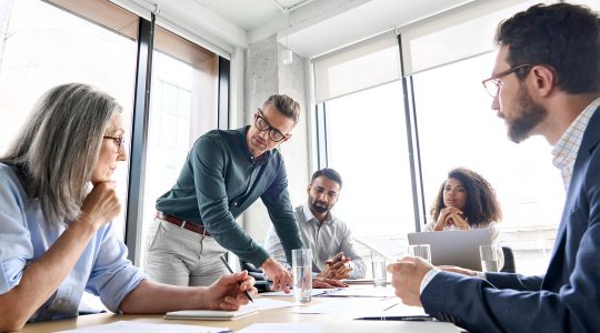 Five businesspeople discuss ideas around a meeting table.