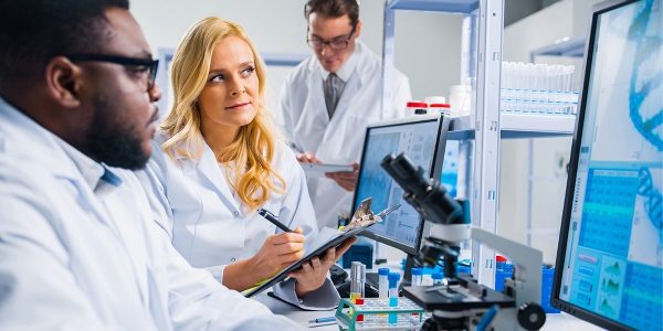 Two scientists in lab coats look at data on computer screens.