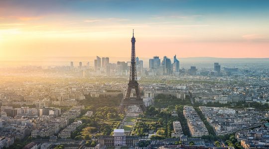 An aerial view of the Paris skyline at dusk, with the Eiffel Tower prominently centered.